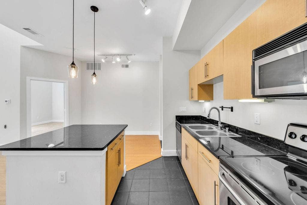 4605 Cedar Springs Road, #327, Dallas, TX 75219 Modern kitchen featuring light wood-finish cabinetry, dark stone countertops, stainless steel appliances, and a built-in microwave