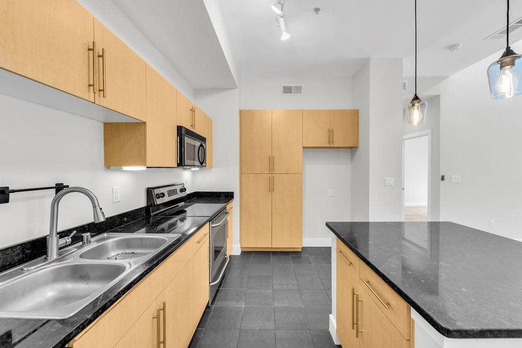 4605 Cedar Springs Road, #327, Dallas, TX 75219 Kitchen featuring dark stone countertops, light wood-finish cabinetry, stainless steel appliances, and dark tile flooring