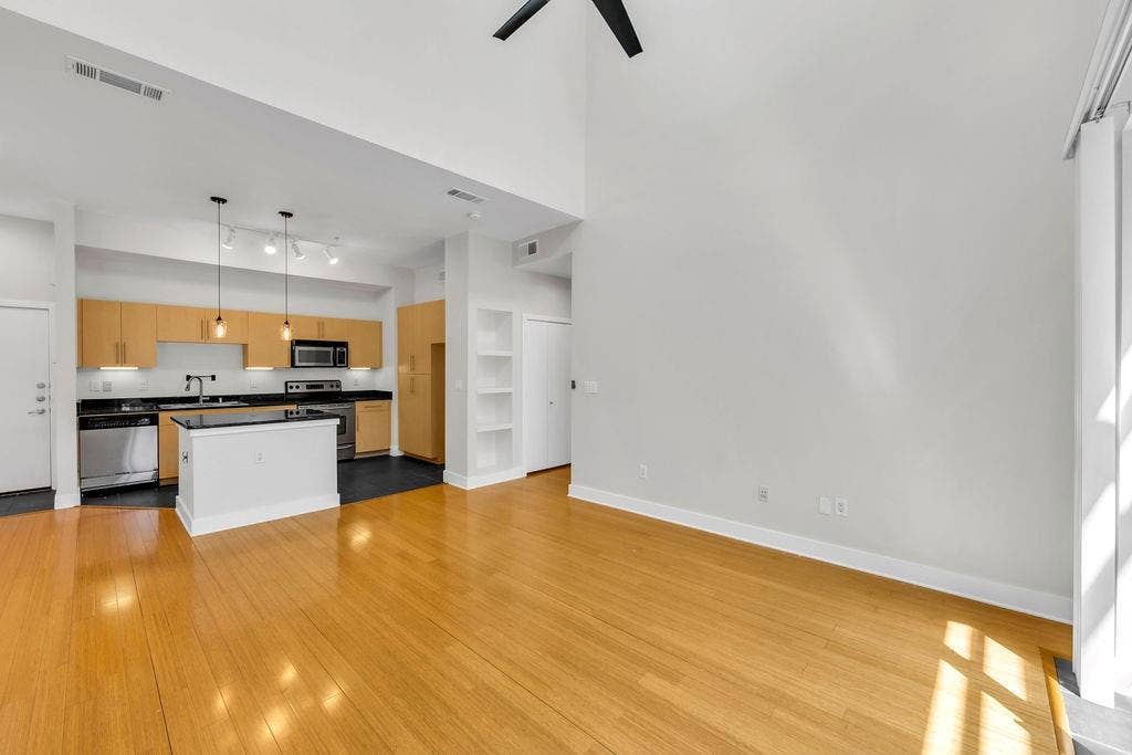 4605 Cedar Springs Road, #327, Dallas, TX 75219 Open-concept living area with high ceilings, wood-finish flooring, and a kitchen featuring stainless steel appliances, dark countertops, and light wood cabinetry