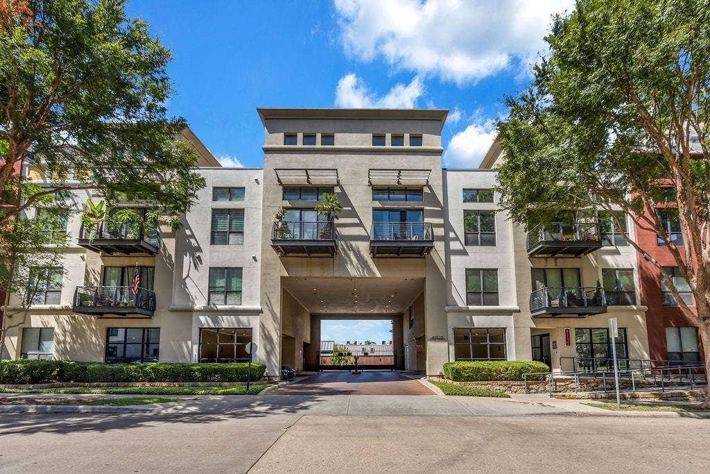 4605 Cedar Springs Road, #327, Dallas, TX 75219 Multi-story building featuring a stucco exterior, multiple private balconies with metal railings, a central drive-through passage, and integrated landscaping