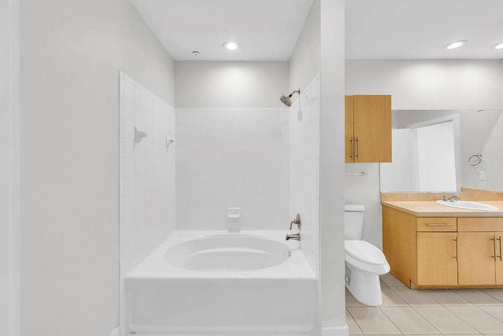 4605 Cedar Springs Road, #327, Dallas, TX 75219 Soaking tub with tile surround, wood-finish vanity with countertop, integrated sink, and wall-mounted mirror