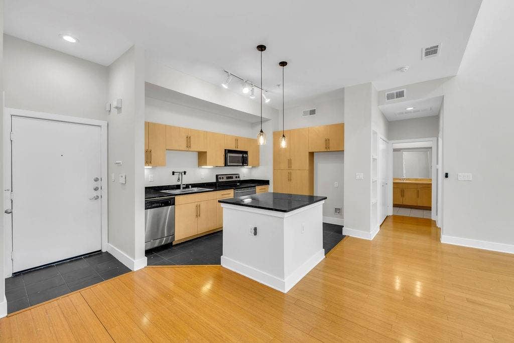4605 Cedar Springs Road, #327, Dallas, TX 75219 Open-concept kitchen featuring wood-finish cabinetry, stainless steel appliances, a center island with a dark countertop, and pendant lighting