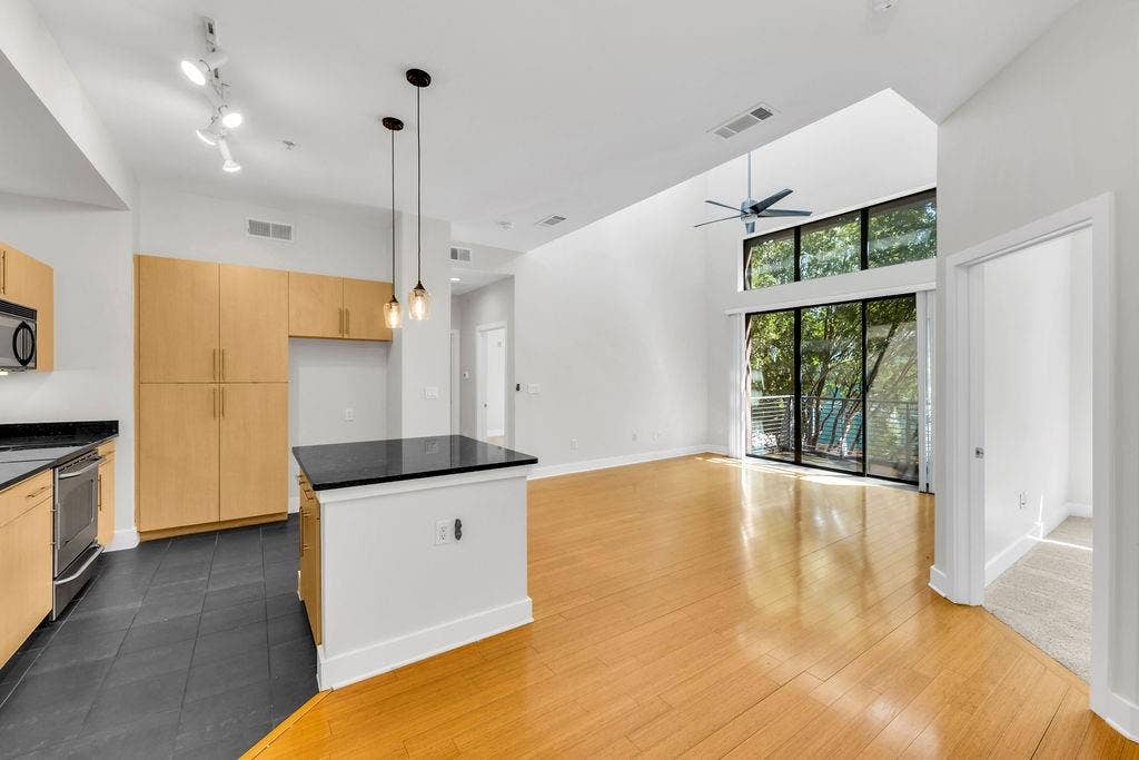 4605 Cedar Springs Road, #327, Dallas, TX 75219 Open-concept living area with high ceilings, wood-finish flooring, a kitchen island with a dark countertop, and large windows with a sliding glass door