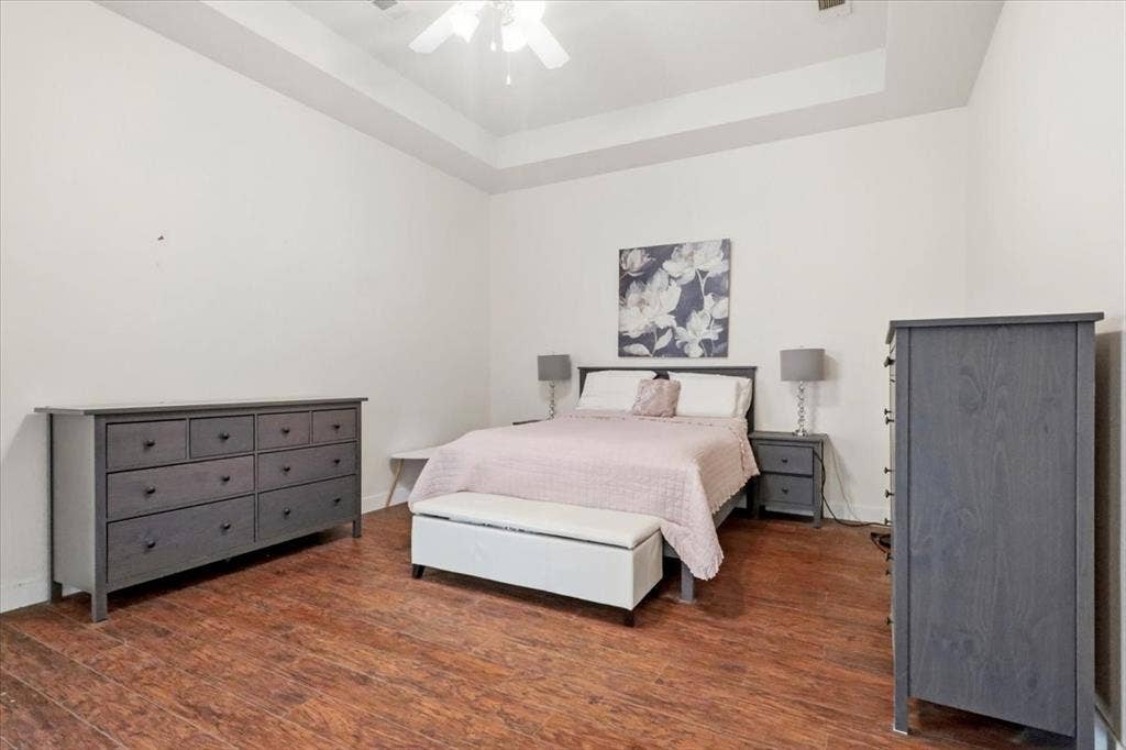Tray ceiling with a ceiling fan, wood-finish flooring, and white walls