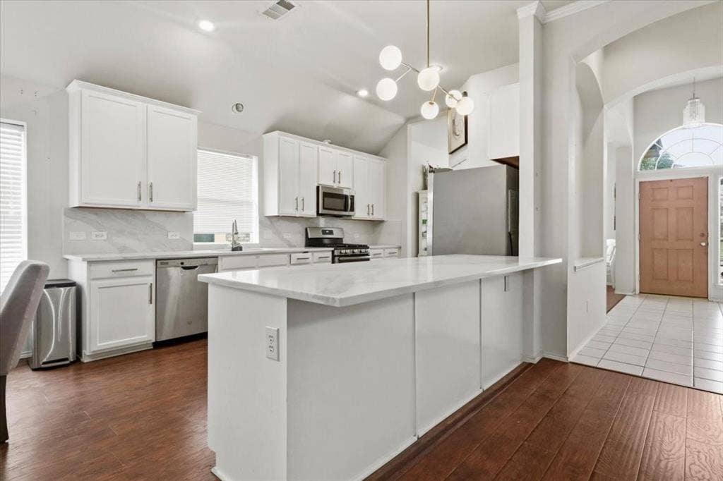 Kitchen featuring white cabinetry, stainless steel appliances, a center island with a light-toned countertop, and wood-finish flooring