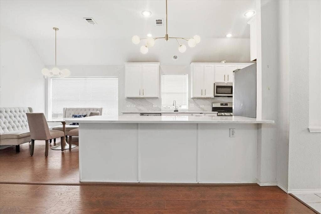 Open-concept kitchen featuring white cabinetry, stainless steel appliances, a white island, and wood-finish flooring