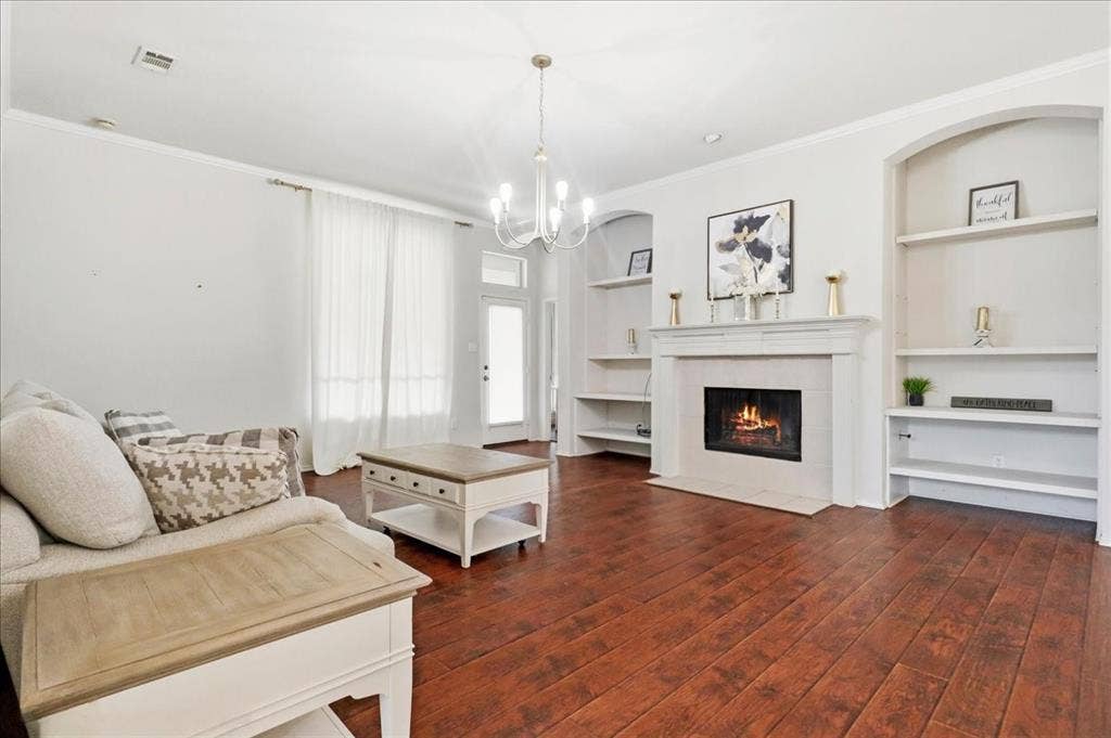 Rich wood-finish flooring, built-in shelving, a fireplace with a mantel, and crown molding