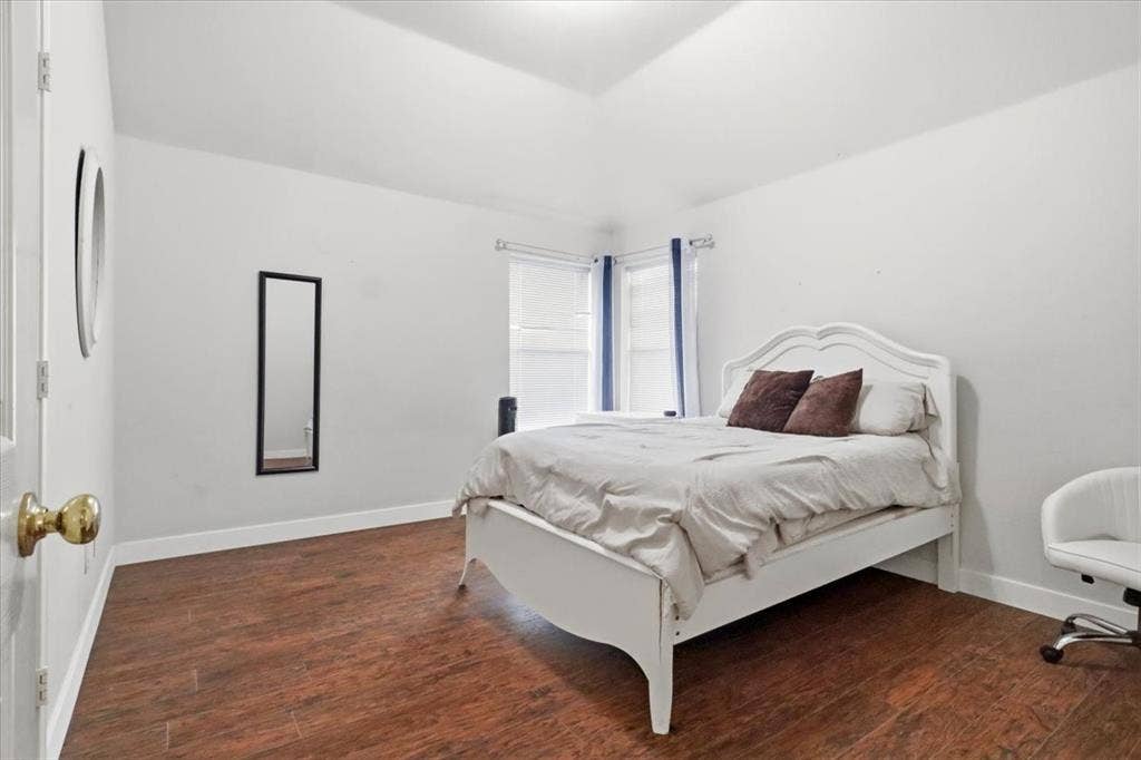 Vaulted ceiling, wood-finish flooring, white walls, and window with blinds
