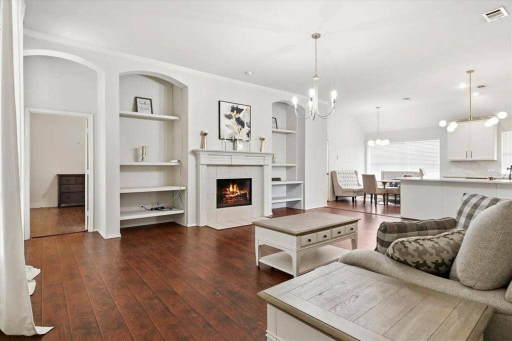 Wood-finish flooring throughout, featuring a fireplace with a white mantel, built-in shelving, and archways