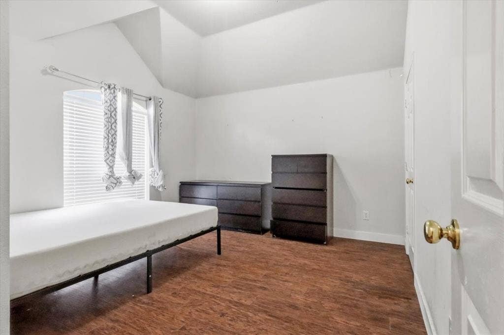 Vaulted ceiling, wood-finish flooring, white paneled door with brass hardware, window with blinds