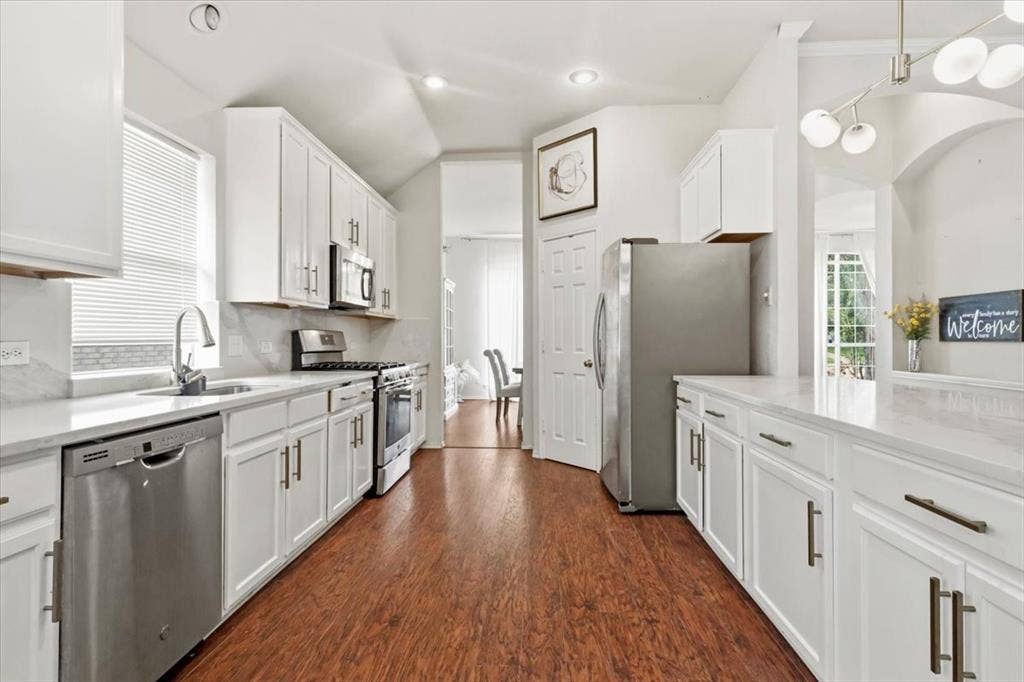 Kitchen featuring white cabinetry with brushed nickel hardware, stainless steel appliances, light-toned countertops, and wood-finish flooring
