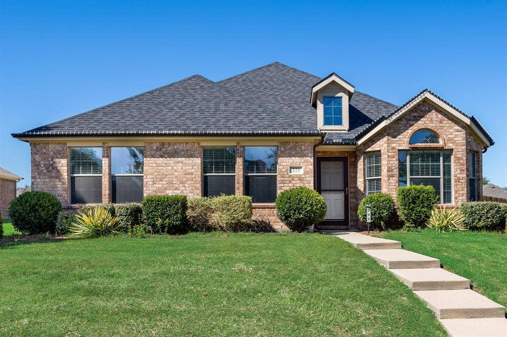 221 Cliffbrook Drive, Wylie, TX 75098 Brick exterior with a dark shingle roof, featuring a dormer window and arched transom window