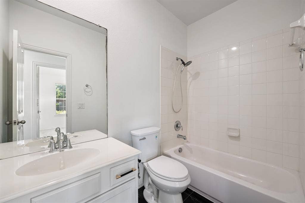 221 Cliffbrook Drive, Wylie, TX 75098 White vanity with integrated sink, chrome faucet, wall-mounted mirror, white toilet, and a white tiled shower/tub combination