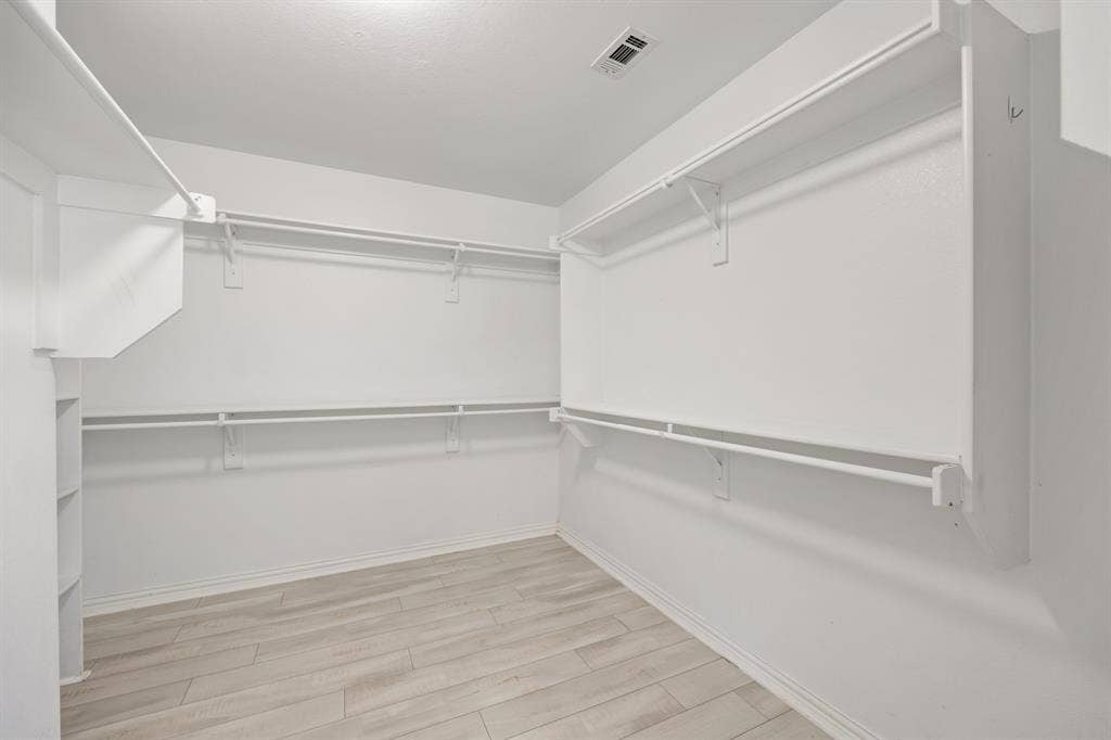 221 Cliffbrook Drive, Wylie, TX 75098 Spacious walk-in closet featuring white wood-finish flooring, built-in shelving, and multiple hanging rods