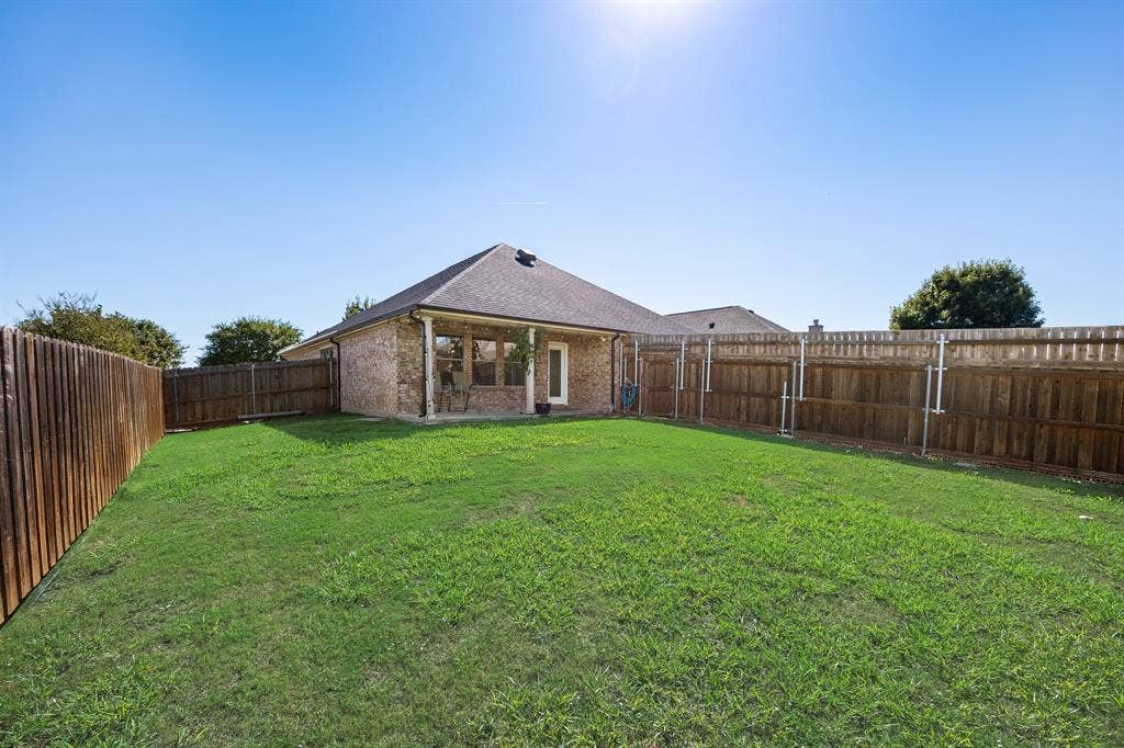 221 Cliffbrook Drive, Wylie, TX 75098 Expansive backyard with a manicured lawn, full privacy fencing, and a covered patio area