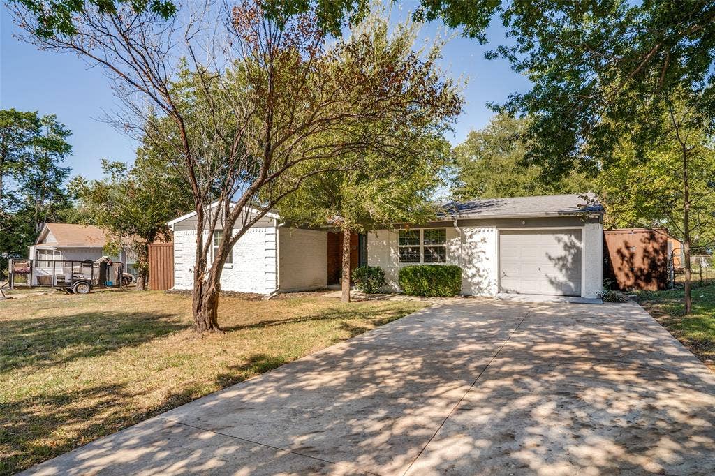 3209 Karla Drive, Mesquite, TX 75150 White painted brick exterior with a gray garage door, a concrete driveway, and established trees