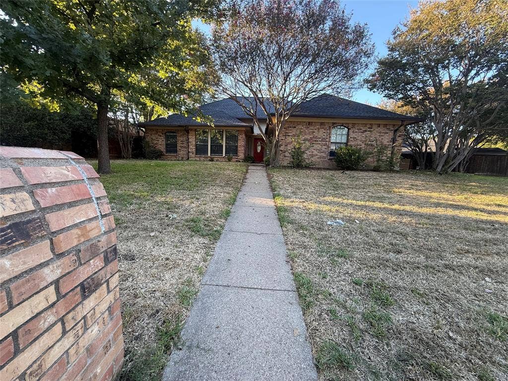 3407 Ruidoso Drive, Arlington, TX 76017 Brick exterior with a red entry door, framed by mature trees, a concrete pathway, and an expansive front lawn