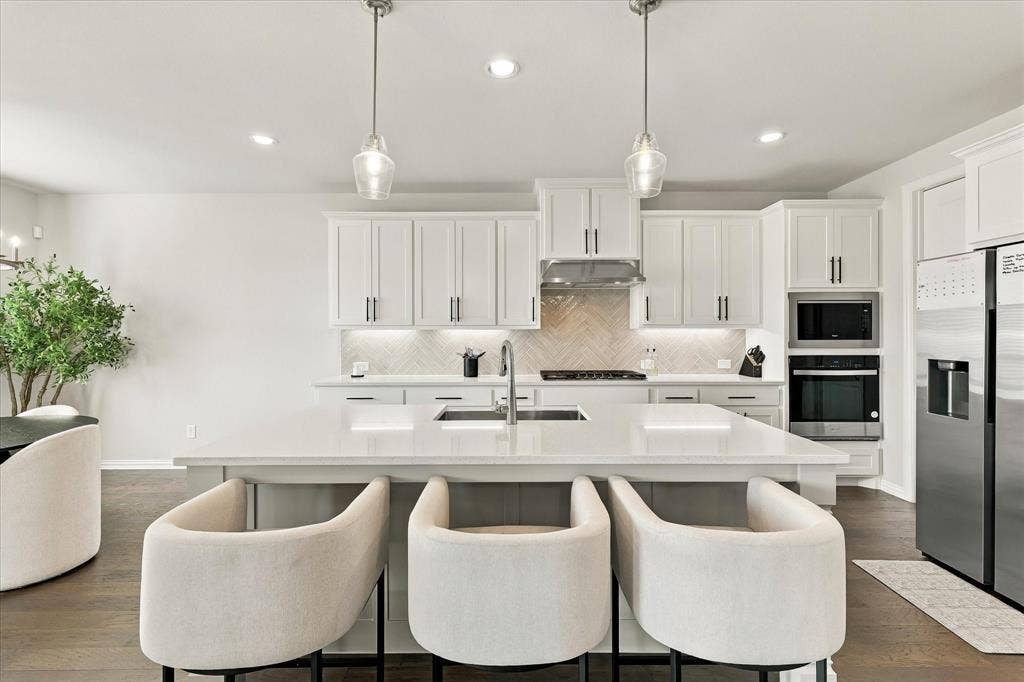 White shaker cabinetry, stainless steel appliances, herringbone tile backsplash, recessed lighting, and a kitchen island with pendant lighting