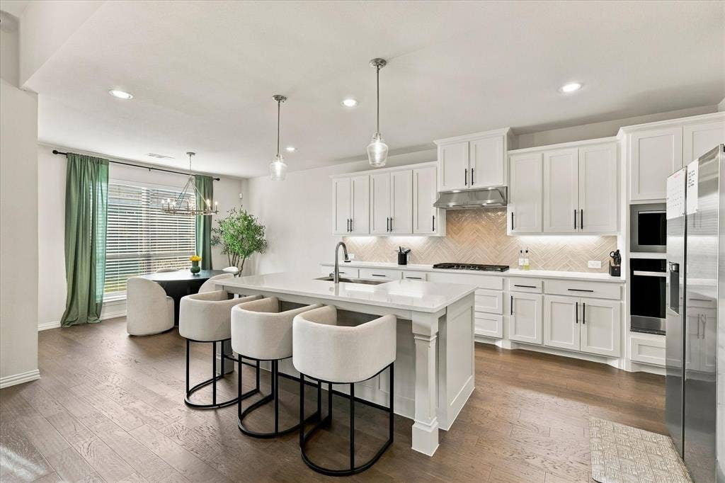 Kitchen featuring a large island with a countertop, shaker cabinetry, stainless steel appliances, a tile backsplash, and wood-finish flooring