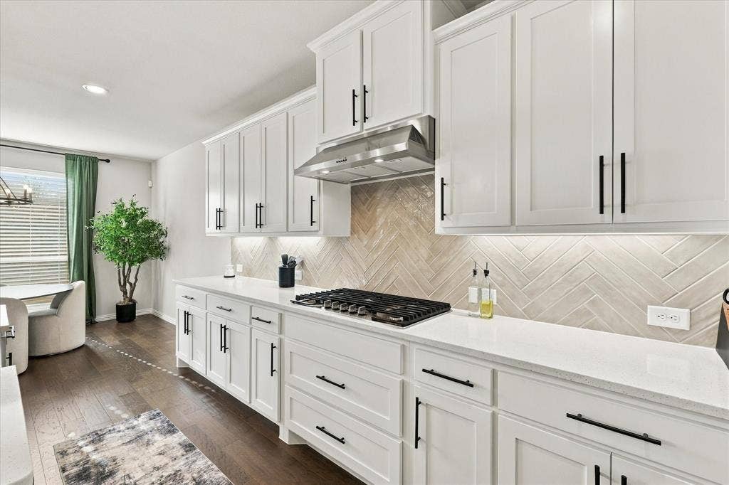 White shaker cabinetry with matte black hardware, quartz countertops, herringbone pattern tile backsplash, stainless steel range hood, and wood-finish flooring
