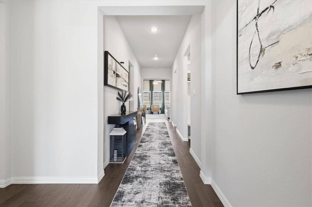 Elongated hallway with dark wood-finish flooring, recessed lighting, and bright white walls