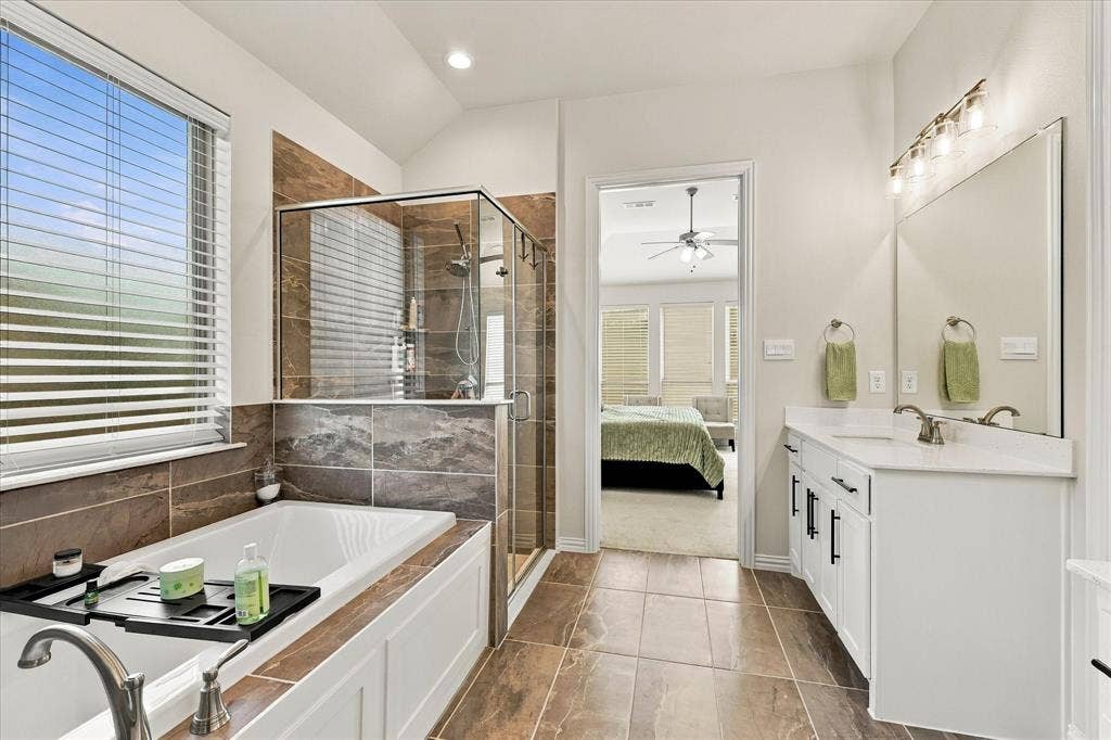 Spacious bathroom featuring a white vanity with under-sink storage, a large mirror, a separate tub, a glass-enclosed shower, and tile flooring