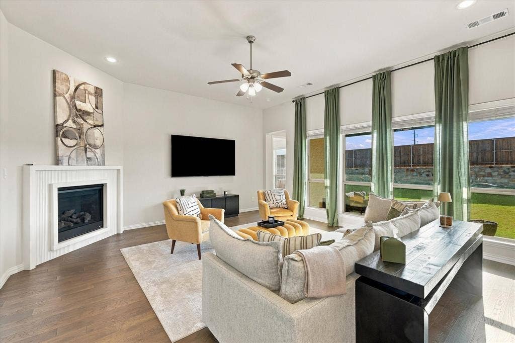 Spacious living area featuring wood-finish flooring, a white fireplace, a ceiling fan, and large windows with roller shades