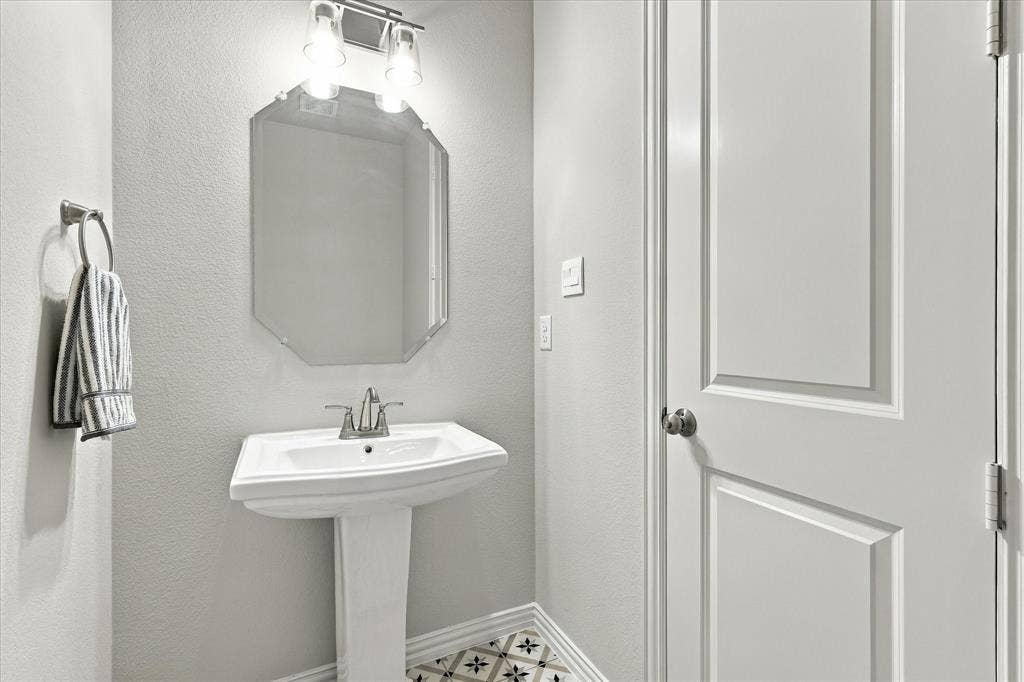 Pedestal sink with chrome faucet, octagonal wall mirror, and decorative patterned floor tile