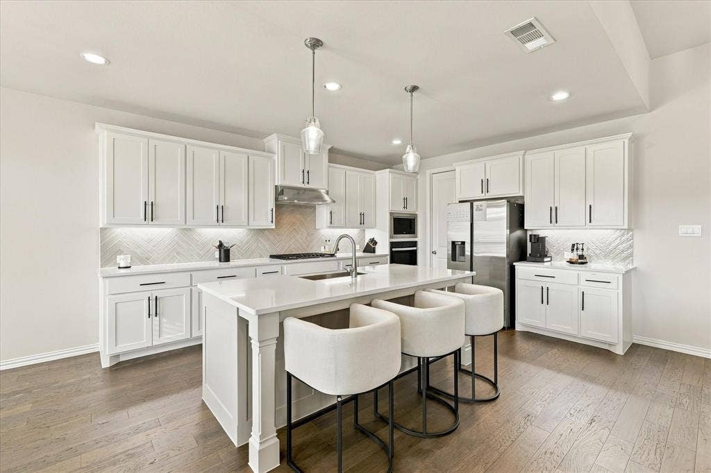 Bright kitchen featuring white shaker cabinetry, an island with solid surface countertops, stainless steel appliances, wood-finish flooring, and recessed lighting