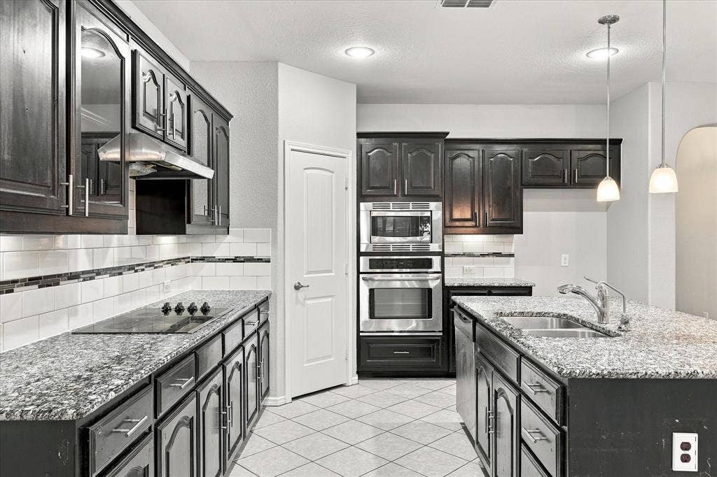 4716 Kendrick Peak Way, Fort Worth, TX 76244 Kitchen featuring dark wood cabinetry, granite countertops, tile flooring, stainless steel appliances, and an undermount sink