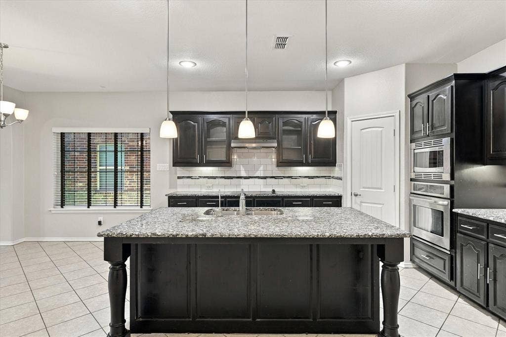 4716 Kendrick Peak Way, Fort Worth, TX 76244 Kitchen featuring an island with a stone-finish countertop, dark wood-finish cabinetry, stainless steel appliances, and tile flooring