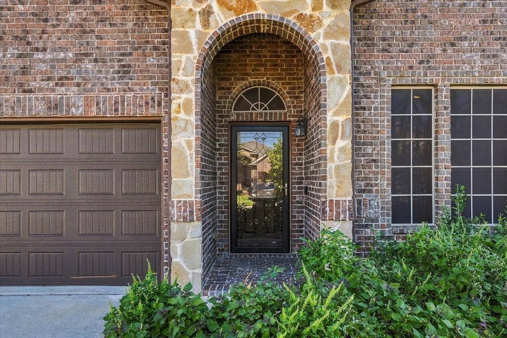 4716 Kendrick Peak Way, Fort Worth, TX 76244 Brick and stone exterior featuring an arched entry, a paneled garage door, and multiple windows with grilles