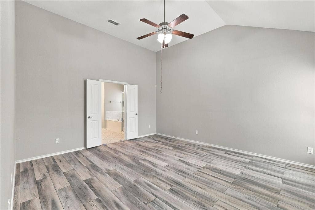 4716 Kendrick Peak Way, Fort Worth, TX 76244 Vaulted ceiling with a ceiling fan, wood-finish flooring, and double doors opening to a bathroom with a built-in tub and a shower enclosure