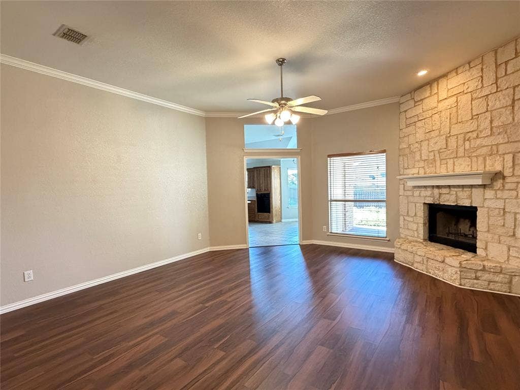 5932 Highcrest Drive, Watauga, TX 76148 Spacious room featuring wood-finish flooring, a stone-clad fireplace with a mantel, crown molding, and a ceiling fan