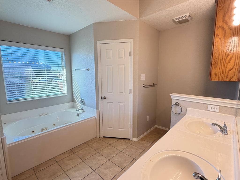 5932 Highcrest Drive, Watauga, TX 76148 Jacuzzi bathtub with a window, dual vanity sinks, ceramic tile flooring, and a wood-finish wall-mounted cabinet