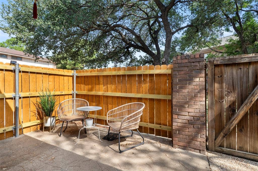 4414 Westminster Drive, Irving, TX 75038 Private courtyard retreat featuring warm wood-finish fencing, mature shade trees, brick architectural detailing, and a gravel surface ideal for outdoor entertaining