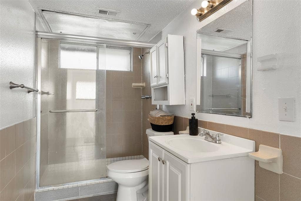 4414 Westminster Drive, Irving, TX 75038 Bathroom featuring a vanity with an integrated sink, a mirrored medicine cabinet, and a shower with a sliding glass enclosure
