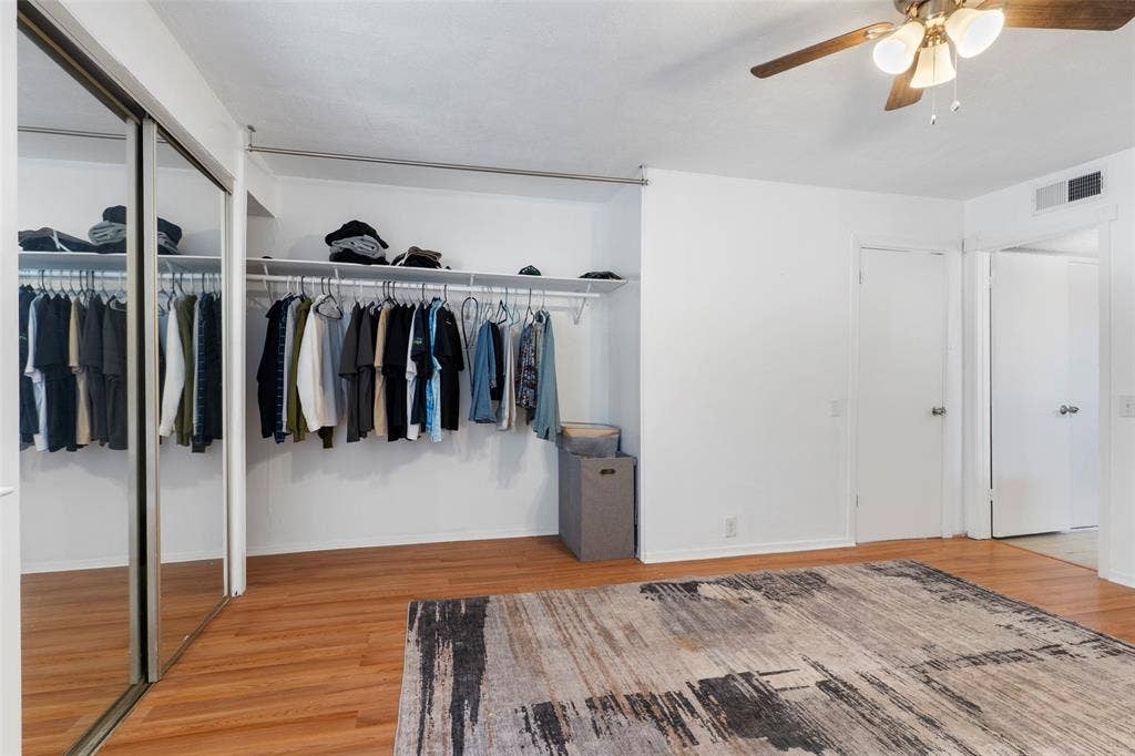 4414 Westminster Drive, Irving, TX 75038 Primary Bedroom Suite with Mirrored Sliding-Door Closet, Hardwood Flooring, and Ceiling FanThis spacious bedroom features a large mirrored sliding-door closet system with extensive hanging storage and overhead shelving
