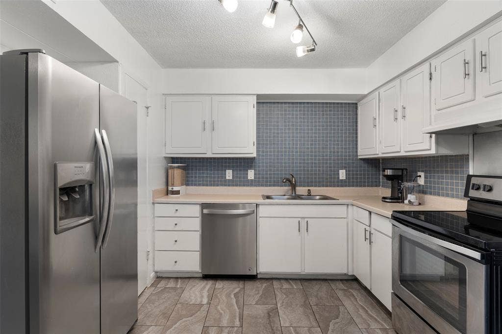 4414 Westminster Drive, Irving, TX 75038 Modern kitchen featuring white cabinetry with chrome hardware, stainless steel appliances including a side-by-side refrigerator and dishwasher, blue subway tile backsplash, wood-finish flooring, and an L-shaped layout with ample counter and storage space