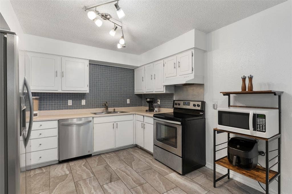 4414 Westminster Drive, Irving, TX 75038 Modern kitchen featuring white cabinetry, stainless steel appliances including a dishwasher and electric range, gray subway tile backsplash, wood-finish flooring, and track lighting
