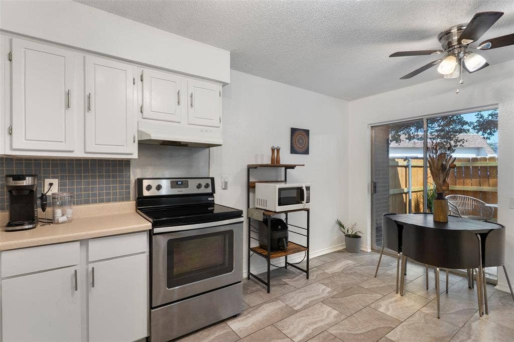 4414 Westminster Drive, Irving, TX 75038 Open-concept kitchen and dining area featuring white cabinetry, stainless steel appliances including a black electric range and oven, light wood-finish countertops, gray tile backsplash, and ceramic tile flooring