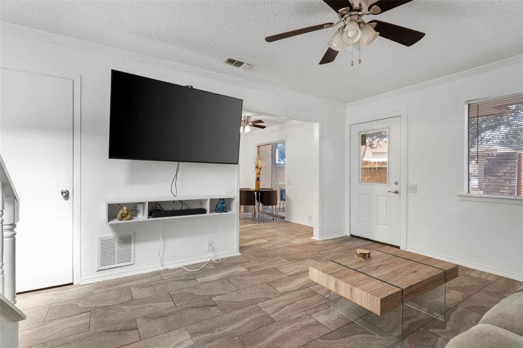4414 Westminster Drive, Irving, TX 75038 Spacious living area featuring a wall-mounted flat-screen television with built-in shelving, wood-finish plank flooring throughout, ceiling fan with integrated lighting, and multiple entry points