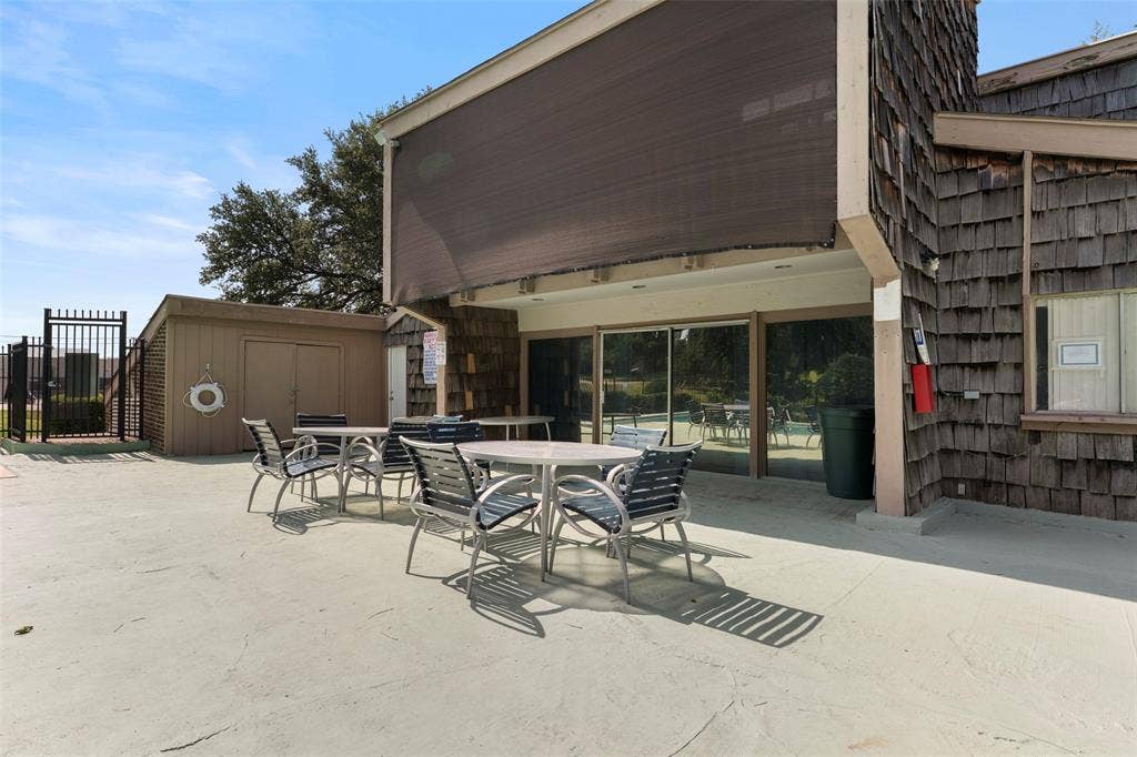 4414 Westminster Drive, Irving, TX 75038 Outdoor patio area with an overhead sunshade, wood shingle siding, an adjacent storage shed, and a black wrought iron fence