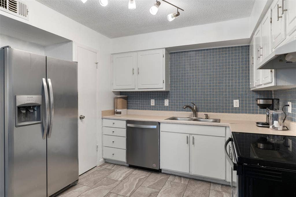 4414 Westminster Drive, Irving, TX 75038 Kitchen featuring stainless steel appliances, white cabinetry, a tiled backsplash, and stone-look flooring