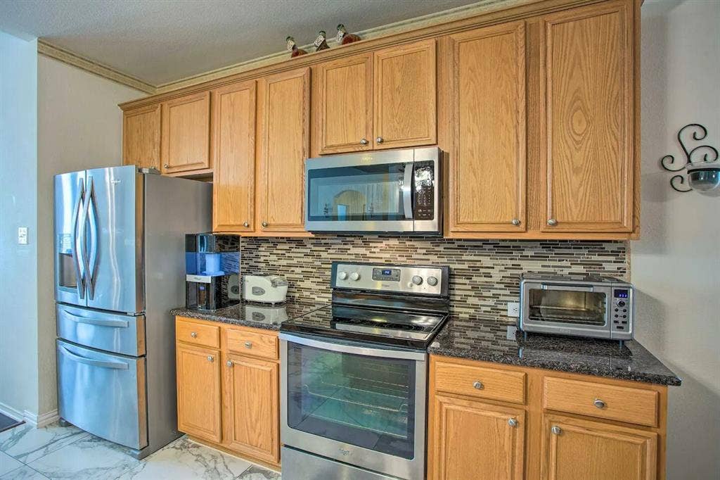 1950 Garrison Way, Garland, TX 75040 Full-height wood-finish cabinetry, black stone-finish countertops, stainless steel appliances, mosaic tile backsplash, and marble-look flooring