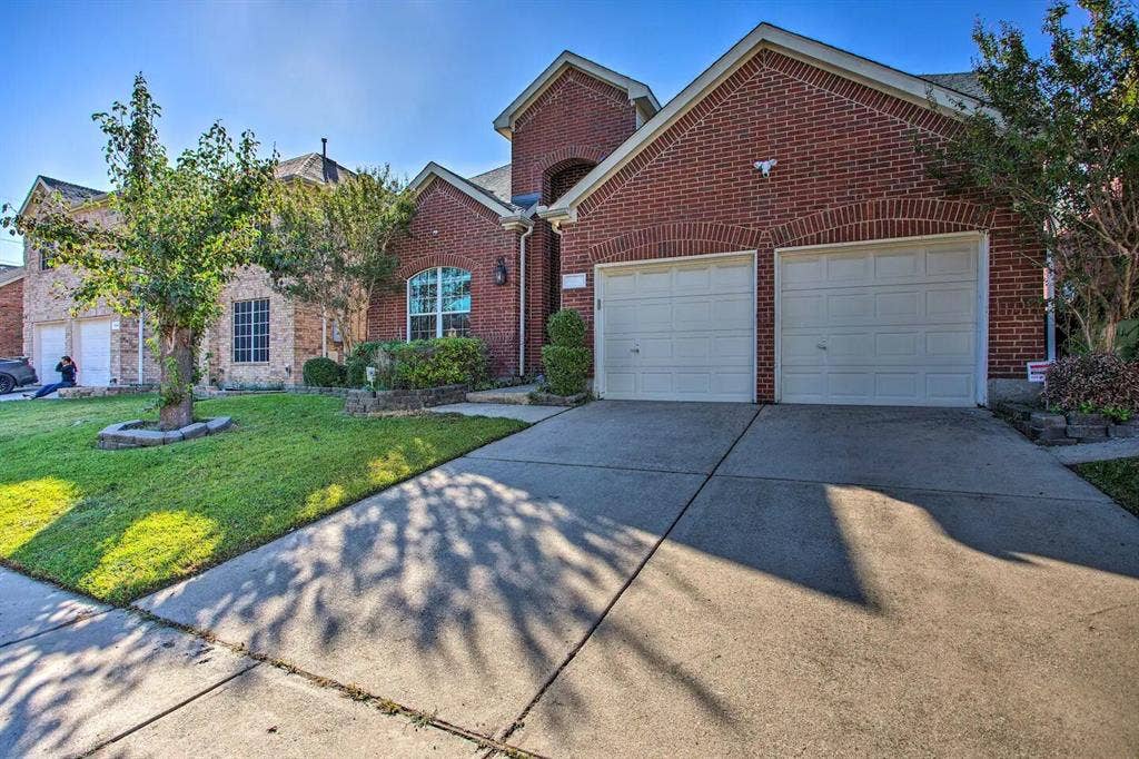 1950 Garrison Way, Garland, TX 75040 Brick exterior with arched window details, two-car garage, concrete driveway, and front lawn with established landscaping