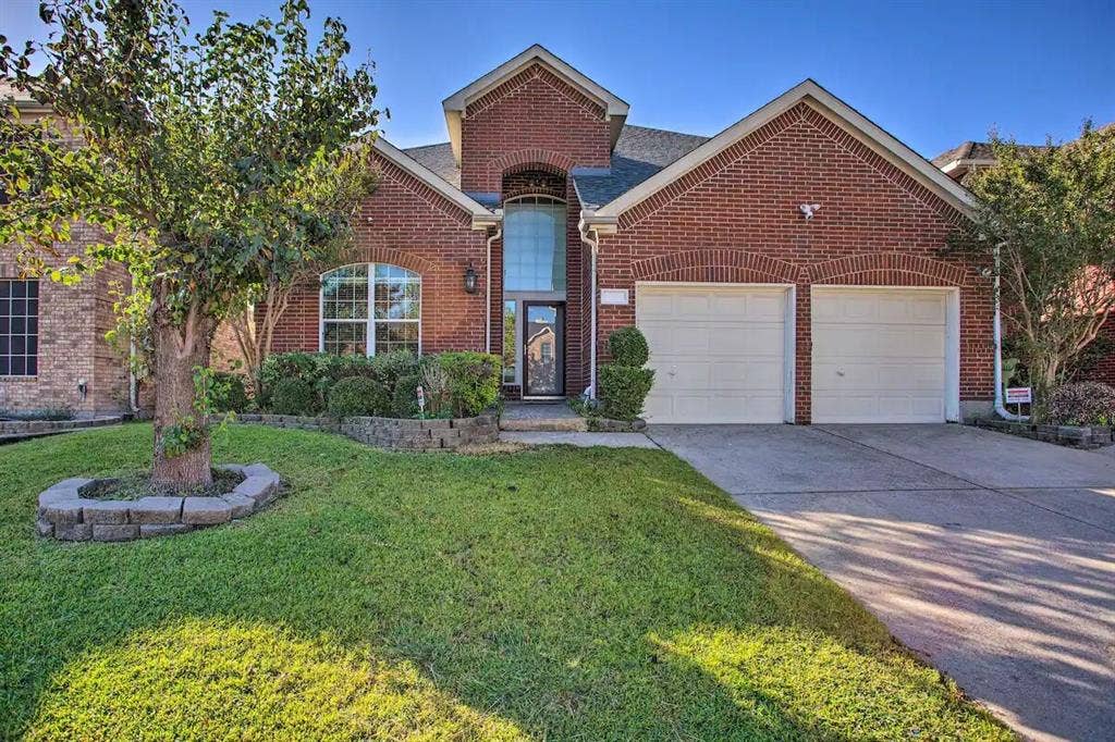 1950 Garrison Way, Garland, TX 75040 Brick exterior with arched window details, two-car garage, established landscaping, and a paved driveway