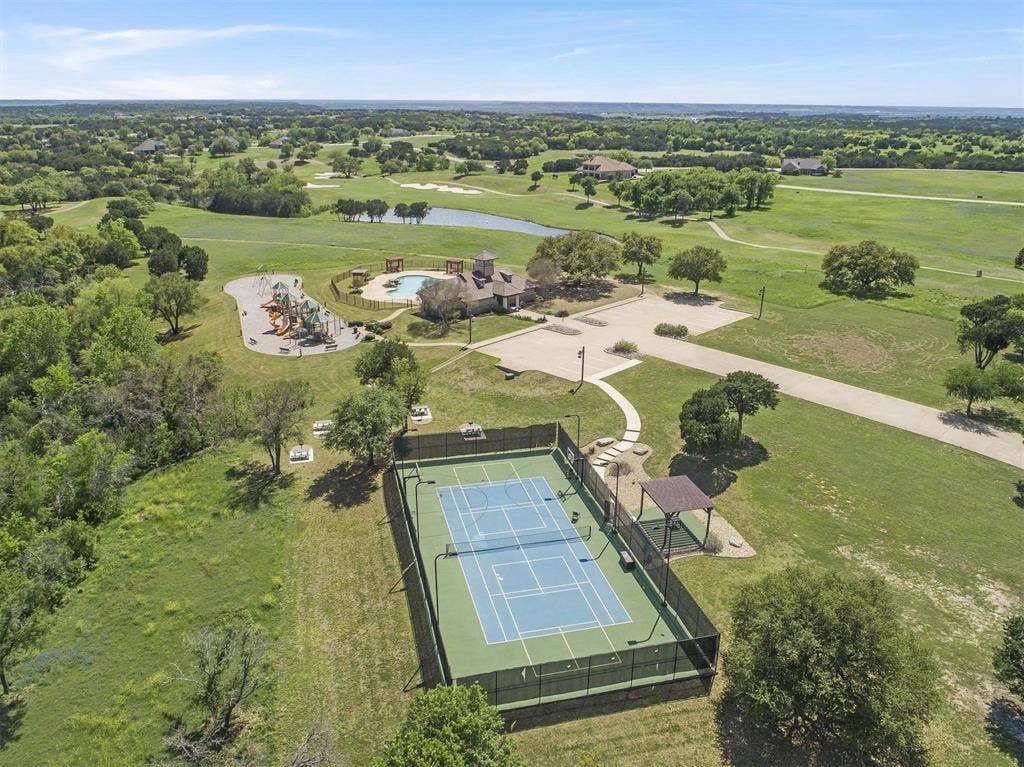 Tennis court with surrounding fencing, adjacent covered seating area, and paved pathways