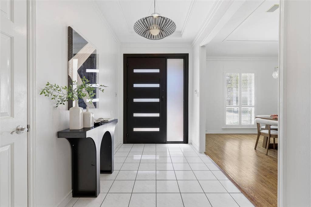 White square tile flooring, modern entryway pendant light, dark wood-finish entry door with frosted glass panels, white interior door, and light wood-finish flooring