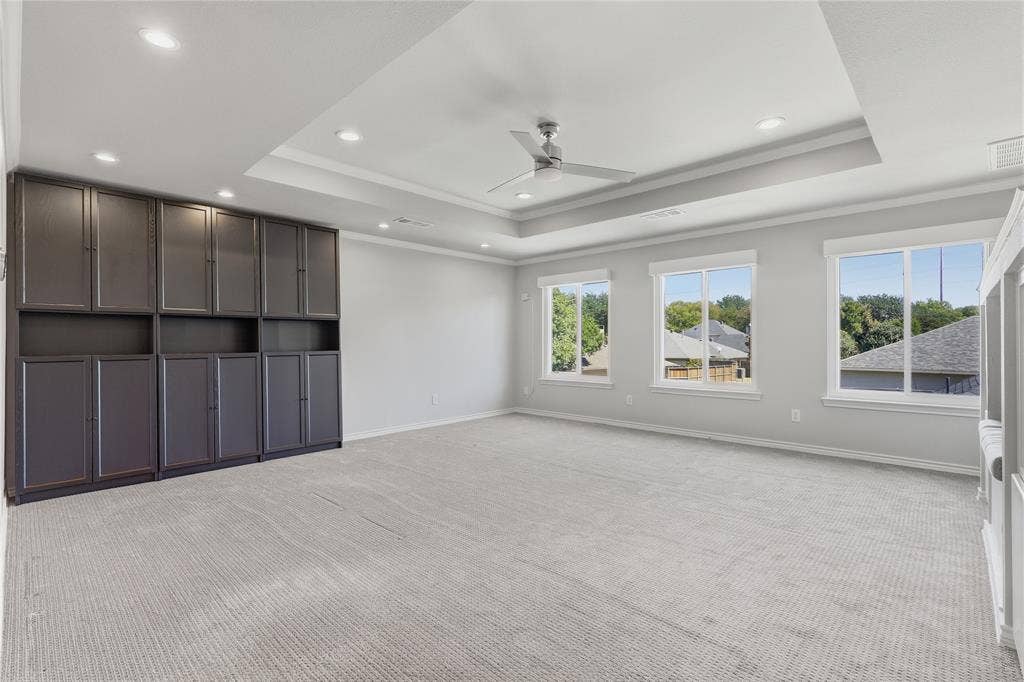 Recessed ceiling lighting, tray ceiling, ceiling fan, built-in cabinetry, and multiple windows